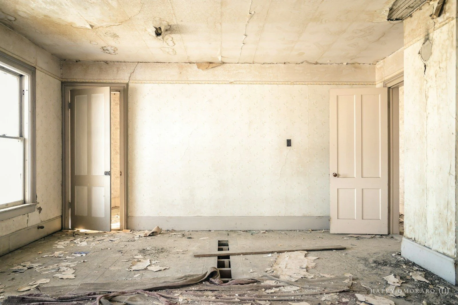 An abandoned room with peeling wallpaper, two open doors and a worn wooden floor