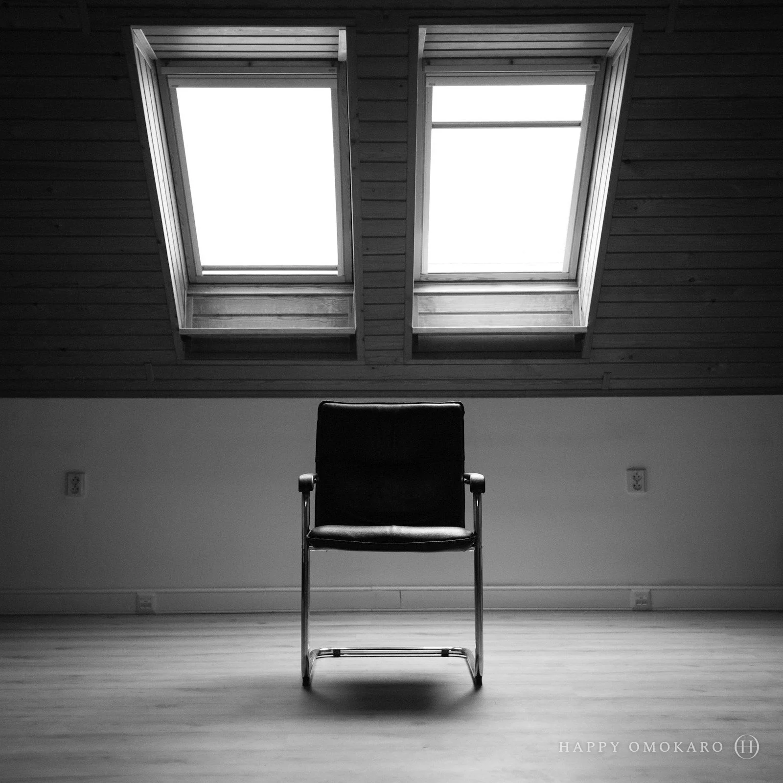 A black and white photograph of a single chair beside a bright window