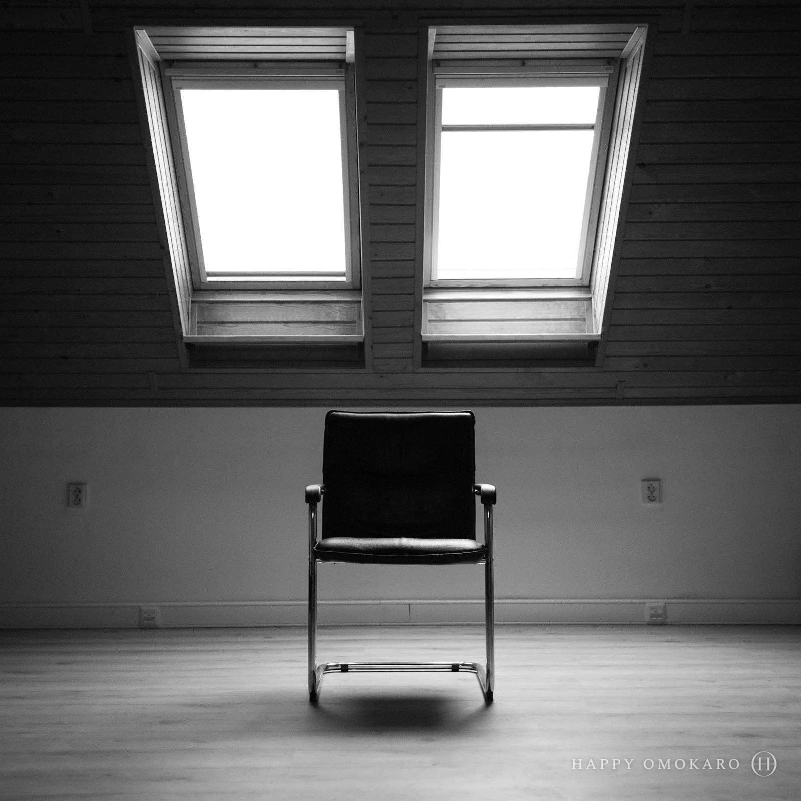 A black and white photograph of a single chair beside a bright window