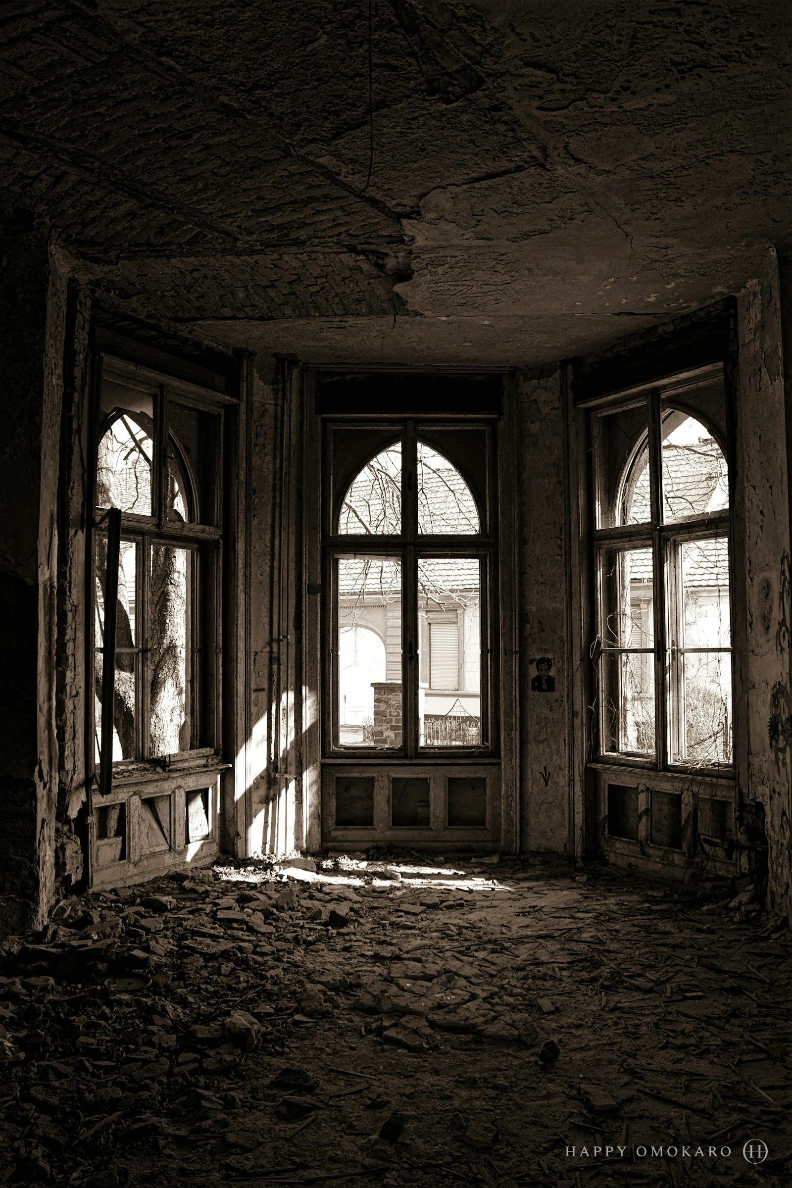 Tall arched windows in an abandoned room, debris scattered beneath them
