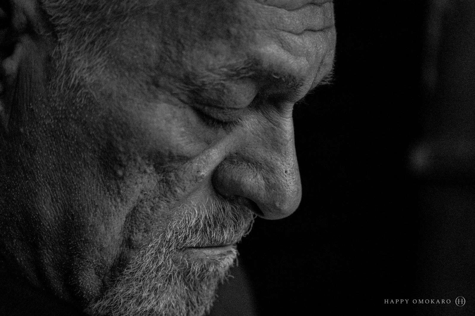 An older man in profile, looking down, photographed in black and white